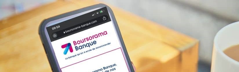 Une femme tient un smartphone pour accéder à son compte bancaire en ligne, incluant Boursorama.