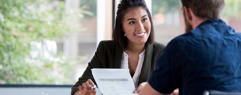 Jeune homme d'affaires inquiet assis à son bureau, tenant une carte de crédit à la main et regardant d'un air contrarié l'écran de son téléphone portable.