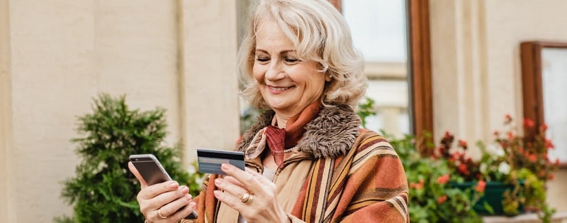 Une belle femme âgée entre les informations de carte de paiement dans un téléphone mobile.