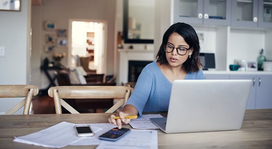 Femme travaillant à domicile devant son ordinateur portable, consultant son téléphone