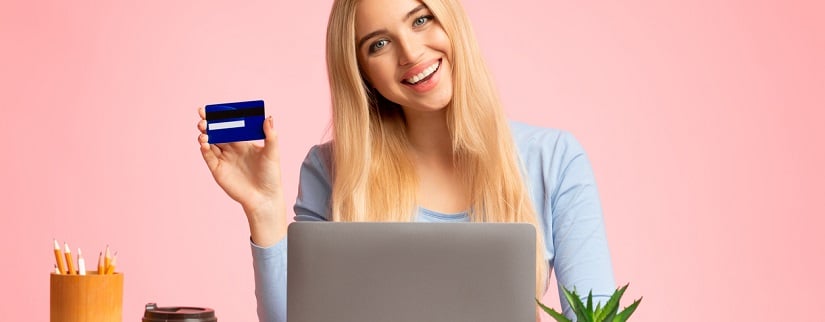 Une jeune étudiante en plein sourire tenant sa carte bancaire après avoir regardé son compte en ligne.