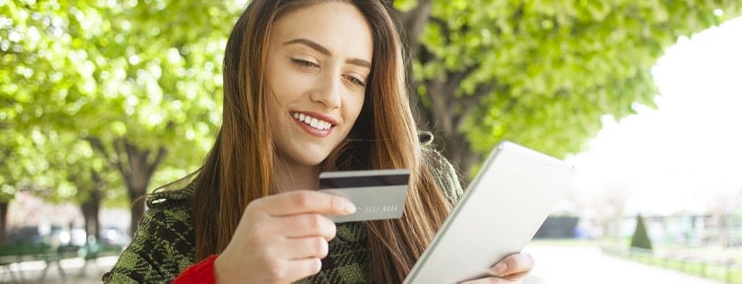 Une jeune fille qui sourit tient une carte de crédit et une tablette
