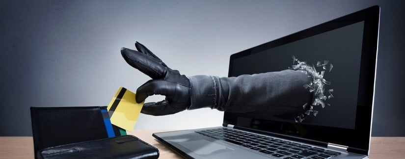 Une main sortant de l'écran du laptop vole la carte de crédit du porte feuille devant le laptop
