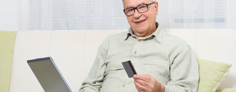 Un homme âgé utilisant un laptop avec une carte de crédit à la main