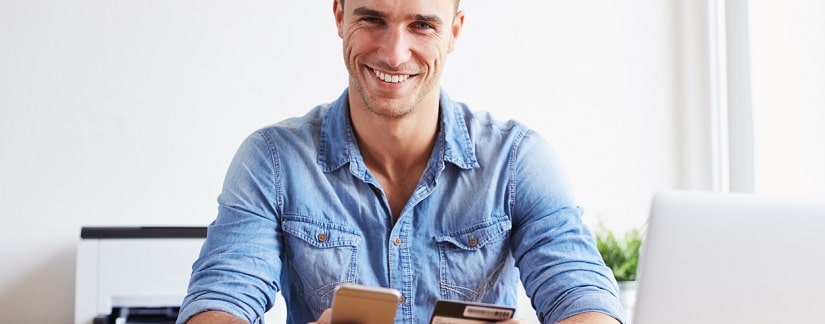 Un jeune homme tenant son smartphone et une carte de crédit