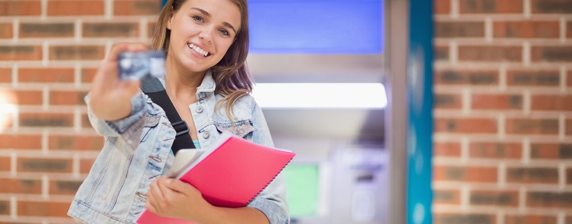 une étudiante devant un distributeur avec sa carte de crédit