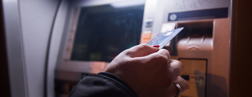 Une personne avec sa carte bancaire devant un distributeur de billets