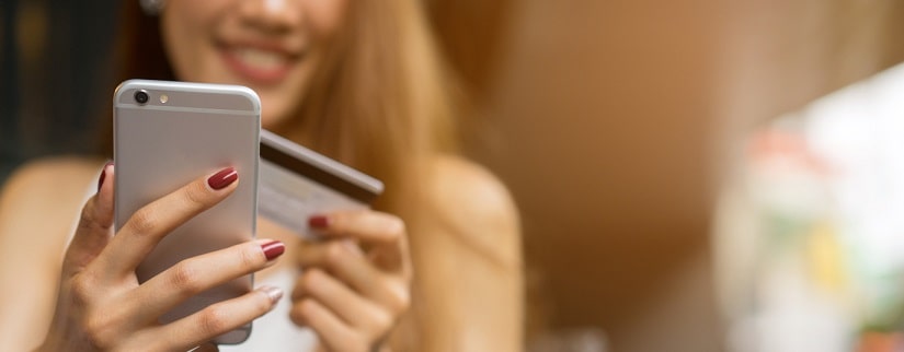 Une femme qui utilise son téléphone en tenant sa carte bancaire 