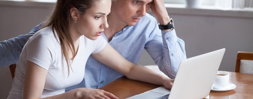 Jeune couple inquiets en  regardent l'écran d'un ordinateur portable en train de lire de mauvaises nouvelles pour leur compte bancaire