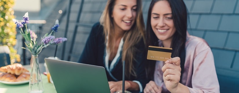 Deux jeunes filles prenant le petit déjeuner sur le toit-terrasse et utilisant une carte de crédit pour faire des achats en ligne