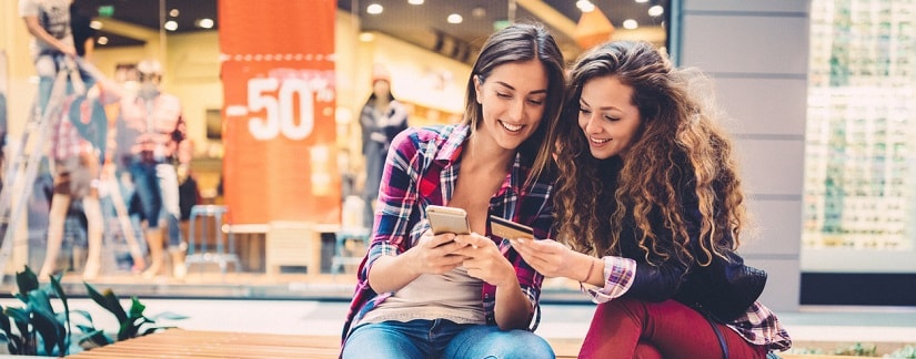 Deux femmes souriantes faire leurs achats en ligne à l’aide d’une carte crédit et d’un smartphone. 