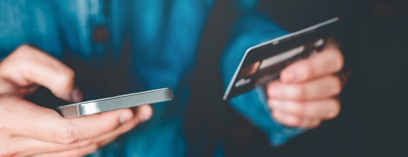 Un homme tenant son smartphone et sa carte bancaire pour faire un paiement en ligne. 