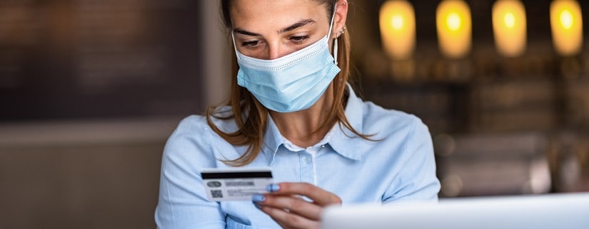 Une jeune femme portant un masque tout en faisant des achats en ligne et paiement par carte de crédit. 