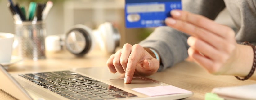 Une jeune femme en tenant sa carte bancaire pour faire un achat en ligne.