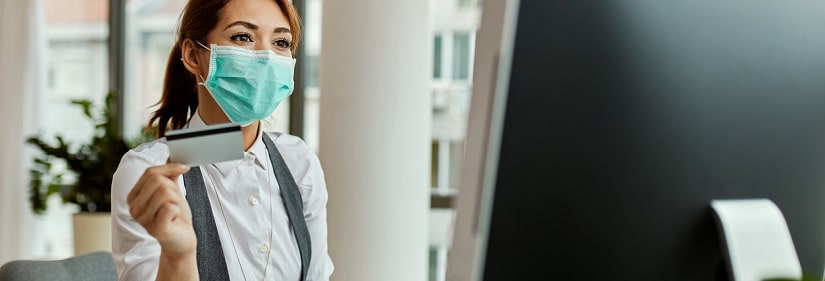 Femme entrepreneur portant un masque facial lors de l'utilisation de la carte de crédit et des achats sur Internet au bureau.