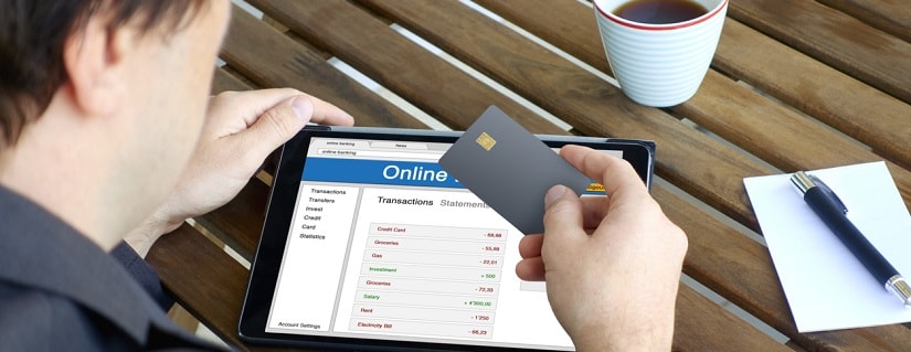 Un homme dans un café tenant sa carte de crédit et son smartphone pour faire un service bancaire en ligne.