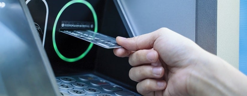Main d’une personne en train de faire insérer sa carte de crédit sur le guichet automatique.