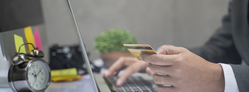 Gros plan d’un homme utilisant un ordinateur portable et tenant une carte de crédit.