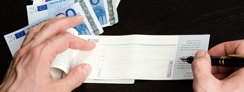 Un homme en train d’écrire la somme d’argent sur son chèque bancaire.