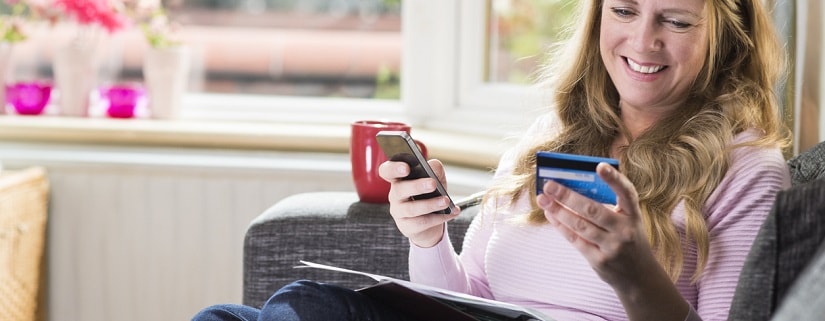 Une femme  tenant sa carte de crédit et son smartphone pour faire un service bancaire en ligne.