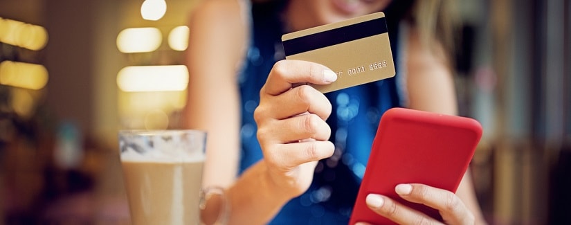 Jeune fille au café en tenant sa carte de crédit et son smartphone pour faire un shopping en ligne. 