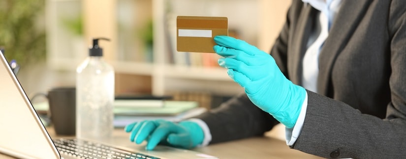 Une femme portant un masque et un gant tenant sa carte de crédit en tapant sur l’ordinateur le service bancaire en ligne.