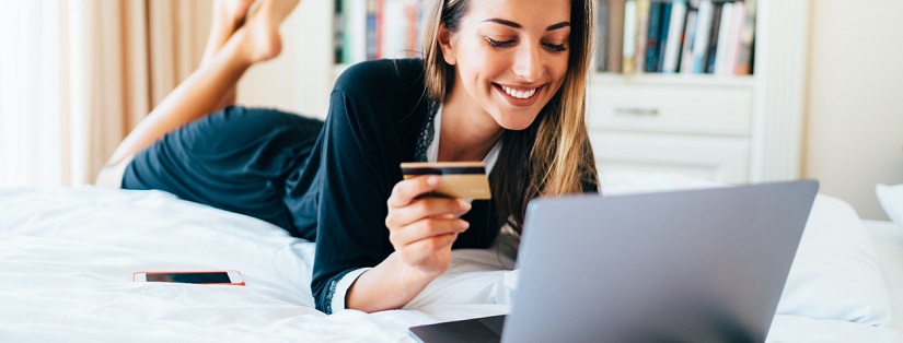 Une jeune femme souriante à la maison à l'aide d'un ordinateur portable et d'une carte de crédit pour les achats en ligne.