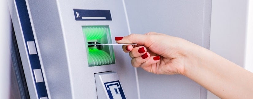 Femme insérant une carte de crédit sur le guichet automatique.