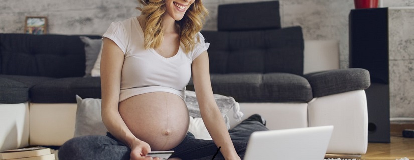 Heureuse femme enceinte assis dans son salon sur le sol et faire des achats en ligne pour son bébé.