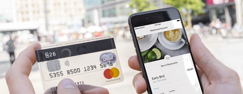 Main d’une personne tenant sa carte de crédit N26 et son smartphone pour faire un achat en ligne.