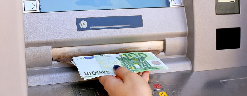 Main de femme tenant de l’argent à un guichet automatique extérieur tenant une poignée de billets de banque
