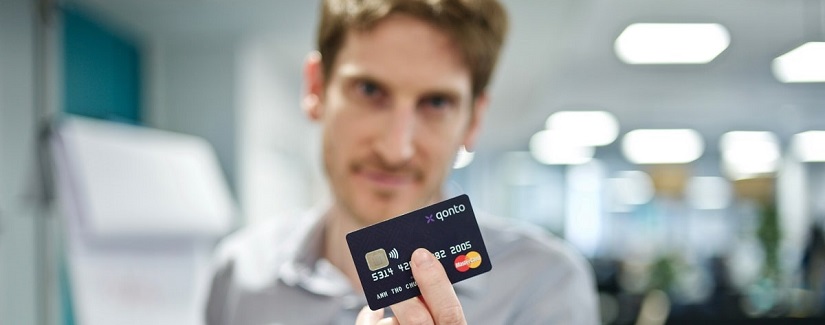 Un jeune homme montre sa carte de crédit Qonto.