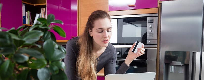 Une belle jeune femme utilisant son ordinateur portable et sa carte de crédit pour faire des achats en ligne ou mobile e-commerce à partir de sa cuisine à l’heure du thé.