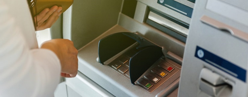Vue de côté de la femme utilisant le portefeuille de ATM tenant une pression sur le numéro de sécurité de PIN sur le guichet automatique de clavier