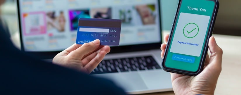 Main d’une personne faisant des achats en ligne avec un téléphone intelligent et une carte de crédit.