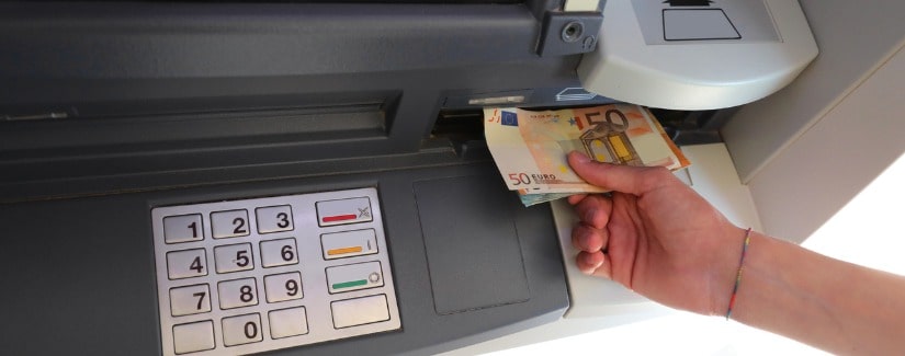 Distributeur automatique de billets avec clavier et main pour ramasser les billets en monnaie européenne.