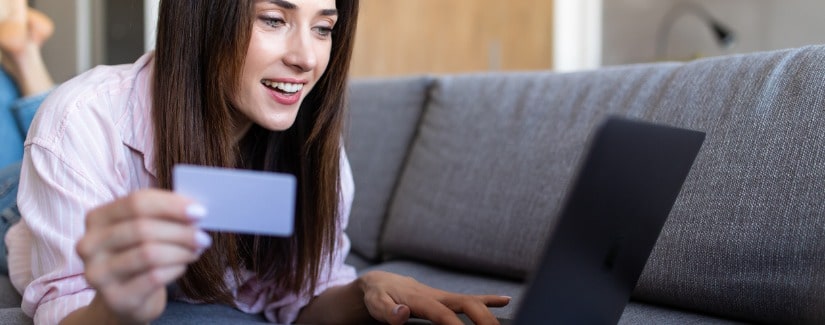 Une jeune femme entre son numéro de carte de crédit sur un site Web allongée sur un canapé