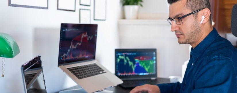 Jeune investisseur homme analyse le marché boursier avec des graphiques sur l’écran de l’ordinateur portable au bureau à domicile