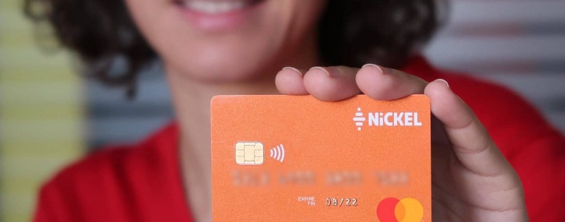 Une jolie femme tenant une carte de crédit Nickel y compris des nouvelles offres.