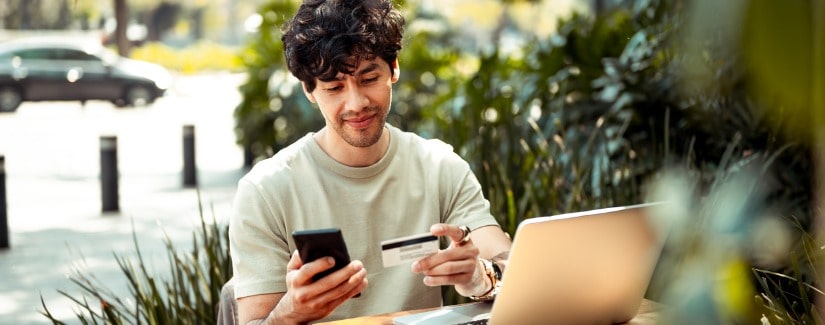 Jeune homme assis au café et payant en ligne avec une carte de crédit.
