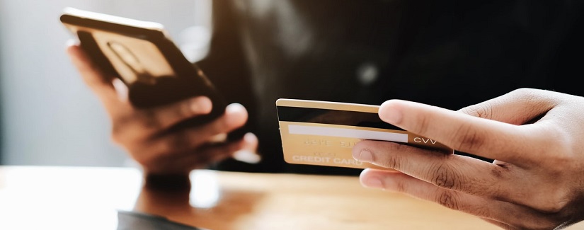 Main d’une personne en tenant sa carte de crédit et son smartphone pour faire un service bancaire en ligne.