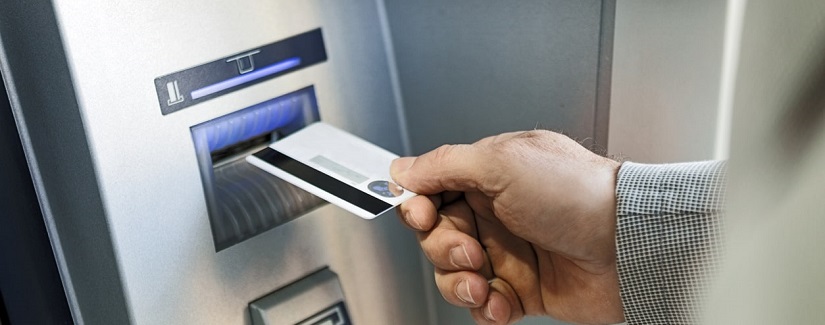 Main d’une personne en train de faire insérer sa carte de crédit sur le guichet automatique pour tirer de l’argent.
