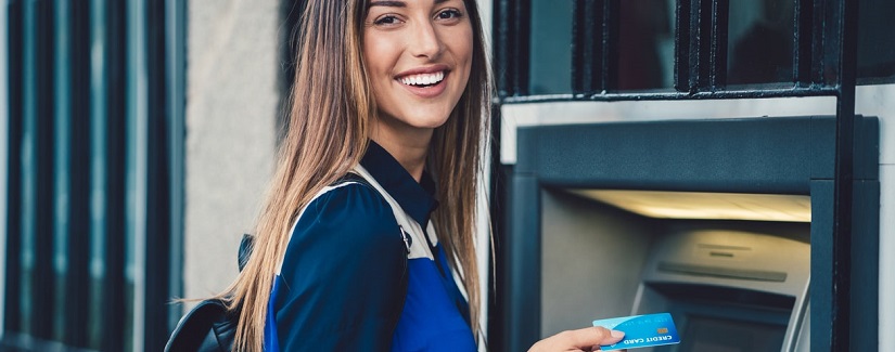 Belle jeune fille tien une carte bancaire devant un distributeur de billet 