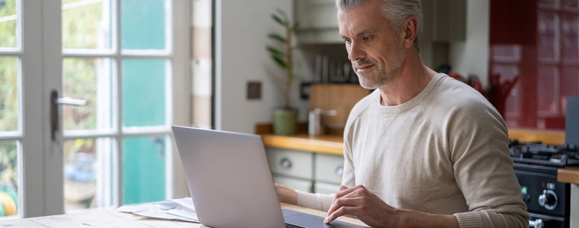Portrait d’un homme adulte travaillant en ligne à la maison sur son ordinateur portable.