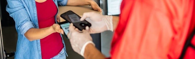 Livreur de pizza vêtu d'une veste rouge lisant le code-barres sur le smartphone du client et effectuant un paiement sans contact rapide et facile.