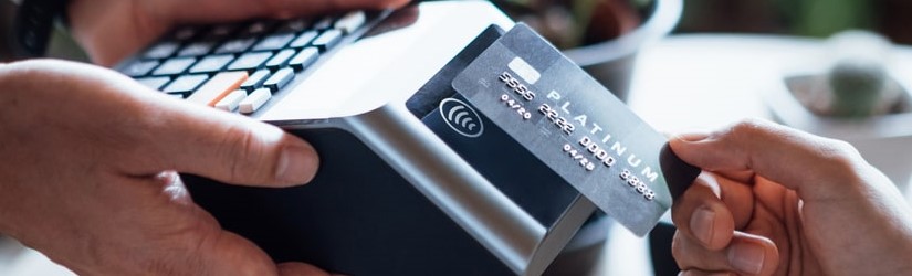 Gros plan de la main d'une femme payant une facture avec une carte de crédit dans un café, en scannant sur une machine à cartes. 