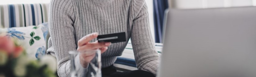 Une jeune femme tenant sa carte de crédit pour faire son paiement en ligne.