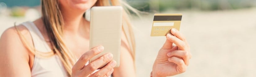 Une belle femme tenant une carte de crédit et un téléphone portable sur la plage pour faire un paiement en ligne.