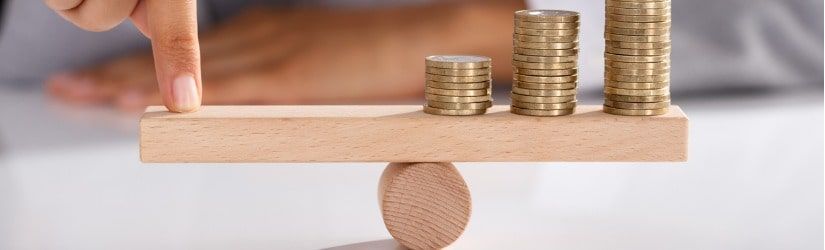 Gros plan du doigt d'un homme d'affaires en train d'équilibrer une pile de pièces de monnaie sur une balançoire en bois.