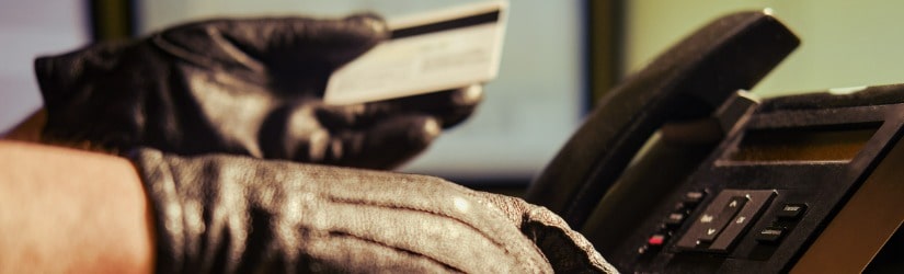 Un homme en gants noirs devant un téléphone fixe avec une carte de crédit en plastique dans les mains, gros plan.